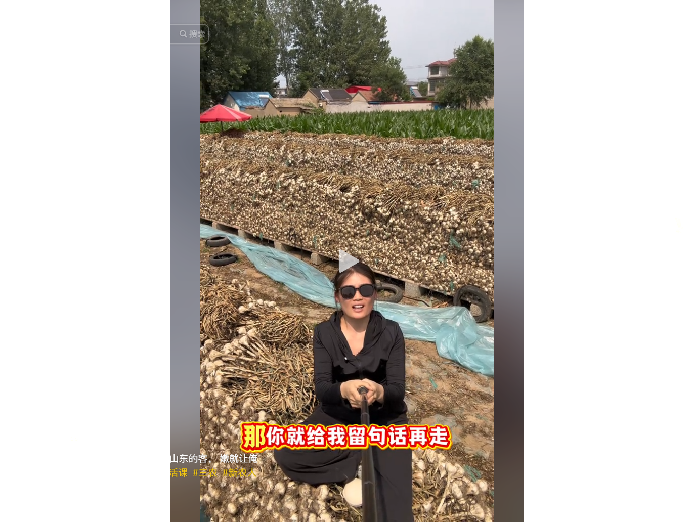 女子在蒜田前手持麦克风，背景堆满大蒜。