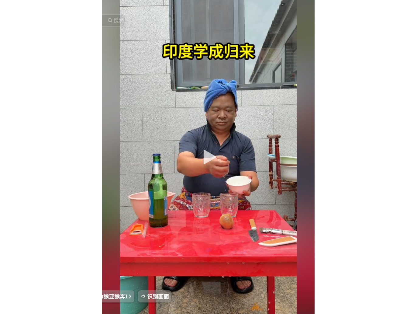 一人头戴蓝色毛巾,坐在红色桌子前,桌上摆放着啤酒瓶、杯子和水果,正在用碗和纸巾操作。