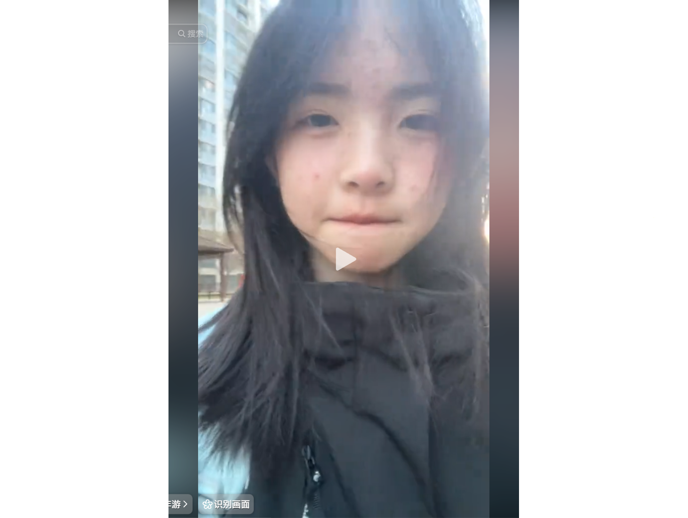 一位年輕女性在戶外自拍，穿著黑色外套，背景為高樓建築。
